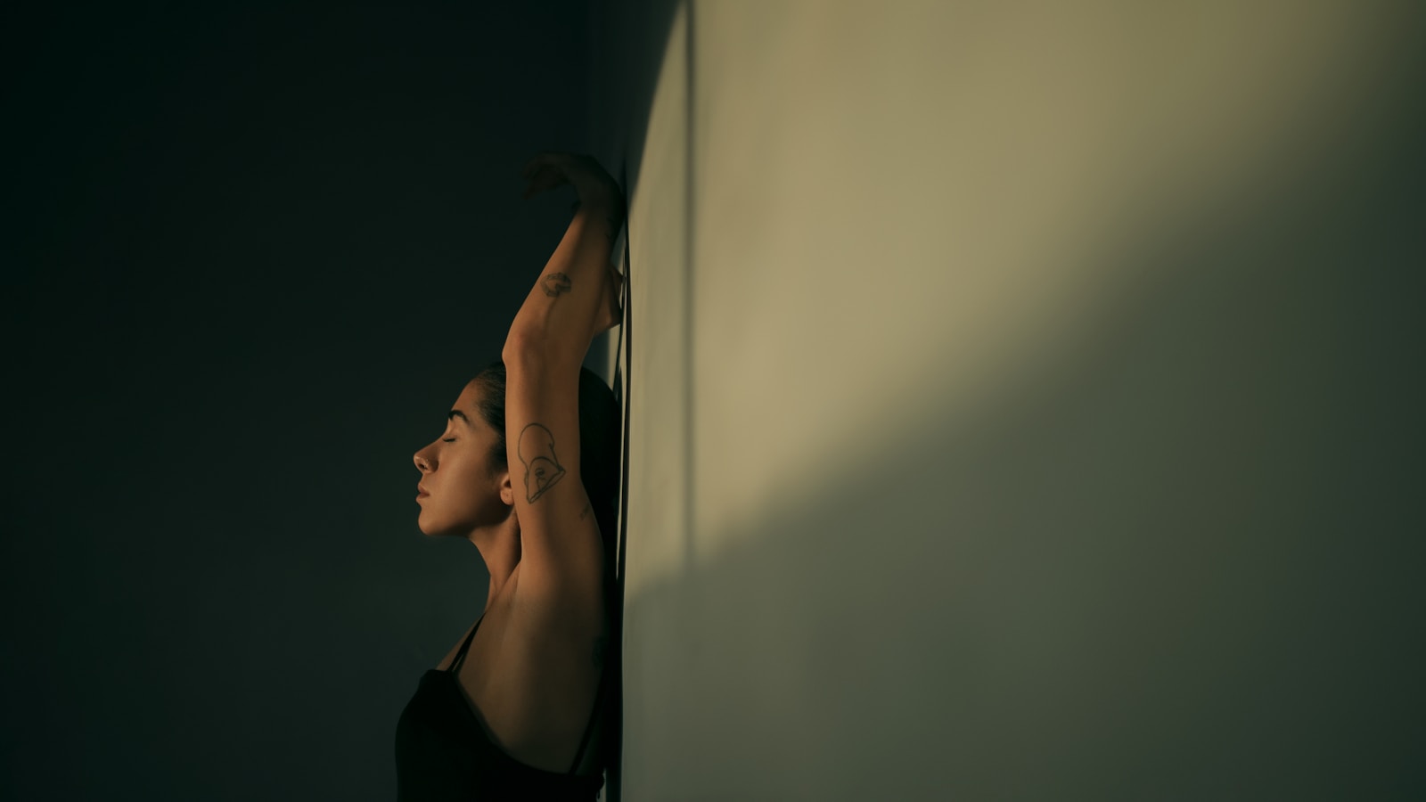 A woman leaning against a wall with her hands behind her head